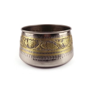 Puede incluir: Un cuenco metálico con acabado plateado que presenta una ancha banda horizontal de metal dorado. La banda dorada está decorada con un patrón de enredaderas florales en relieve, mientras que la sección inferior tiene un sutil diseño de líneas verticales grabadas.