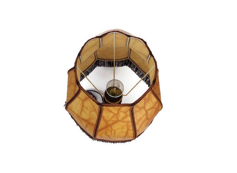 May include: A brown lampshade with a fringe trim and a light bulb inside. The lampshade is made of a textured material that resembles leather.
