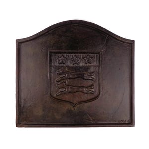 Pode incluir: Uma placa de lareira de ferro fundido castanho escuro com um topo arqueado. O centro apresenta um emblema de escudo em relevo exibindo três estrelas na secção superior e dois cães a correr na secção inferior. O texto 6C8J é visível na parte inferior.