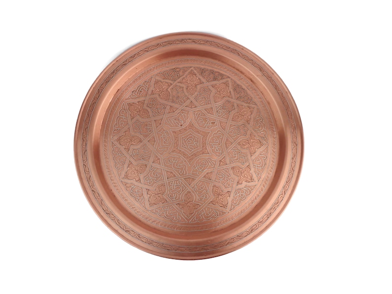May include: A round copper serving tray with an intricate geometric design. The tray has a raised rim and a polished finish.