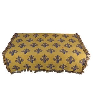 May include: A yellow throw blanket with a blue fleur-de-lis pattern and fringe trim.