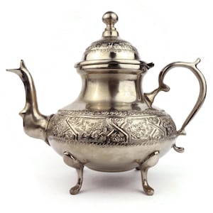 Peut inclure: Une théière en argent avec un design orné et trois pieds. La théière a un couvercle avec un bouton sur le dessus.