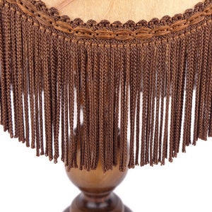May include: A brown lampshade with a fringe trim. The fringe is made of a woven material and hangs down from the edge of the lampshade.