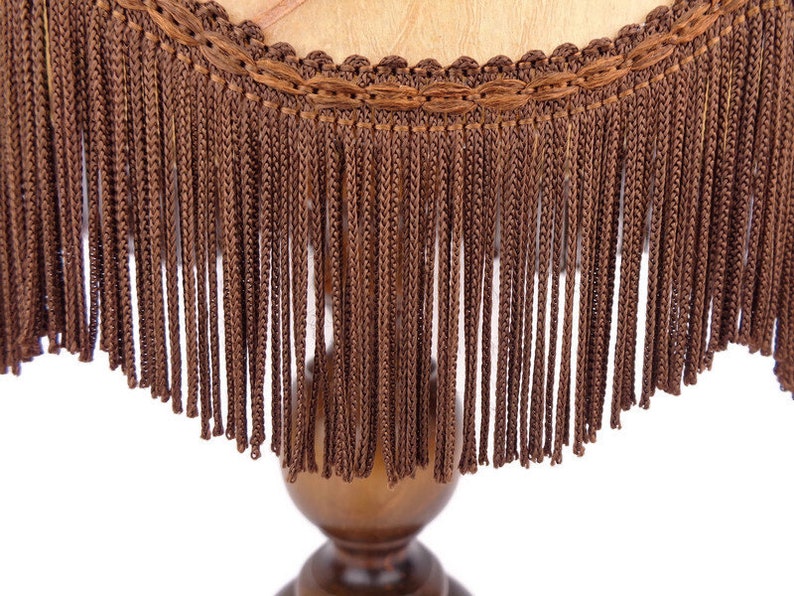May include: A brown lampshade with a fringe trim. The fringe is made of a woven material and hangs down from the edge of the lampshade.