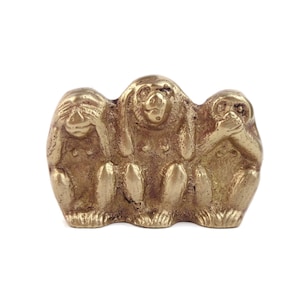 Puede incluir: Escultura de latón dorado que representa a los tres monos sabios: no ver el mal, no oír el mal, no hablar el mal. Los monos están sentados, con las manos cubriendo los ojos, los oídos y la boca. Objeto decorativo.