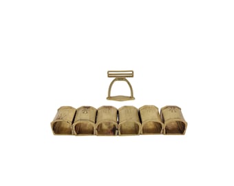 May include: A set of six gold-toned metal napkin rings with a decorative design. The rings are connected by a separate gold-toned metal clasp.