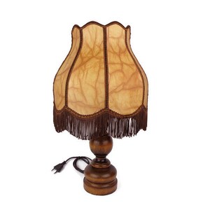 May include: A brown wooden table lamp with a fringed lampshade. The lampshade is made of a light brown fabric with a textured pattern. The lamp has a cord and plug.