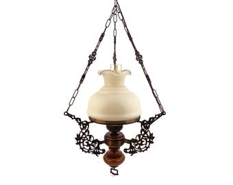 May include: A vintage-style hanging lamp with a white glass shade and ornate metal accents. The lamp is suspended by a chain and has a brown wooden base.