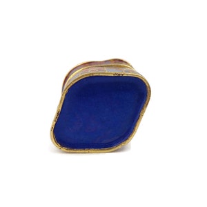 May include: A small, blue and gold enameled box with a geometric design. The box is closed and the top is visible.