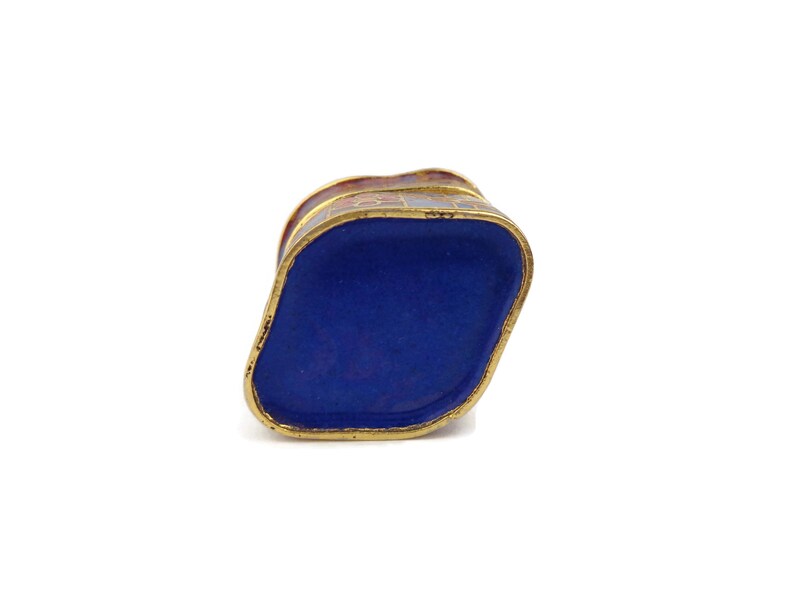 May include: A small, blue and gold enameled box with a geometric design. The box is closed and the top is visible.