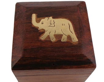 May include: A square, wooden box with a dark brown finish. The top of the box features a gold-colored elephant design. The box is likely used for storing small items, such as jewelry or keepsakes.