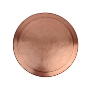 May include: A round copper serving tray with an embossed design. The tray has a smooth, polished surface and a slightly raised rim.