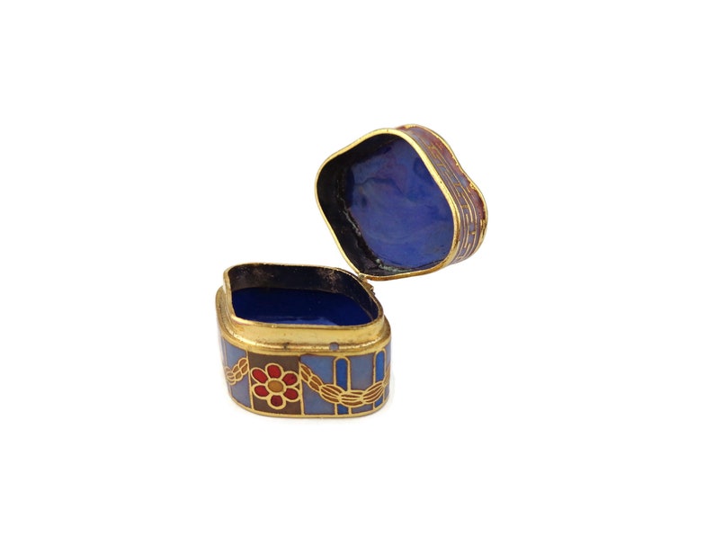 May include: A small, square, decorative box with a hinged lid. The box is made of metal and has a blue, red, and gold enamel design. The inside of the box is lined with blue enamel.