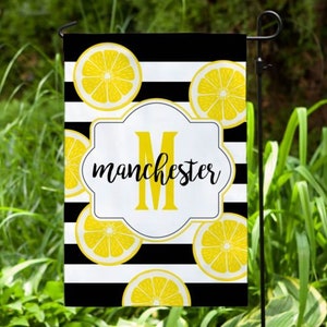 May include: A black and white striped garden flag with yellow lemon slices and the letter "M" in a white circle with the word "manchester" in black script.