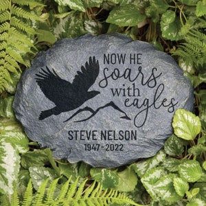 May include: A gray stone memorial with the text "Now he soars with eagles" and "Steve Nelson 1947-2022". A black silhouette of an eagle is flying above a mountain range.