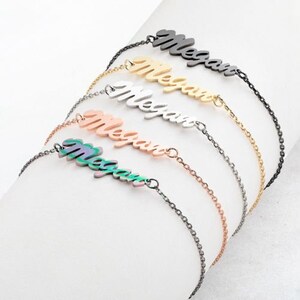 May include: Five silver necklaces with the name "Megan" spelled out in different colors. The necklaces are layered on top of each other, with the black nameplate on top.