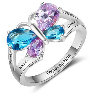 May include: A silver butterfly ring with four blue and purple gemstones. The ring has an inscription that reads "Name1", "Name2", "Name3", "Name4", and "Engraving Here".