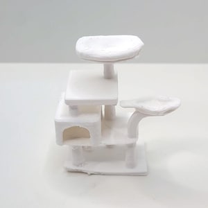 Puede incluir: Un árbol para gatos en miniatura impreso en 3D de color blanco, con un diseño de varios niveles que incluye una pequeña cueva cerrada en la base, una plataforma cuadrada central y dos perchas circulares elevadas sobre postes delgados.