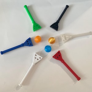 May include: Six colourful plastic scoops with holes, designed for picking up small balls. The balls are green, blue, orange, and gold.