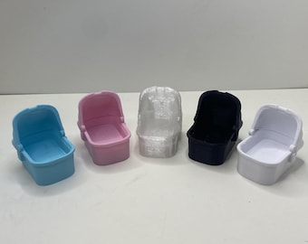 May include: Five miniature baby carriage toys in a row. The carriages are in various colors: light blue, pink, clear, black, and white. Each carriage has a rounded shape with a small interior.