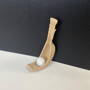 Op de afbeelding: Een beige keramische schep met een witte bal erin. De schep is gevormd als een gebogen lepel met een handvat.