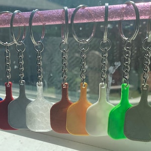 Può includere: Un set di nove portachiavi con ciondoli a forma di pagaia di diversi colori. I ciondoli sono attaccati a catene argentate e anelli portachiavi. I colori dei ciondoli sono blu, rosso, grigio, bianco, arancione, giallo, verde e grigio.