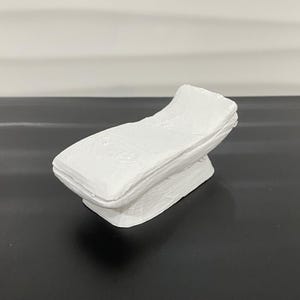 Puede incluir: Una escultura de cerámica blanca de una cama, con un diseño simple y moderno.