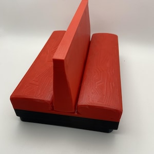 May include: A red and black 3D-printed object with a handle and two rounded sections. The handle is a vertical rectangle, and the rounded sections have a wood grain texture. The base is black.