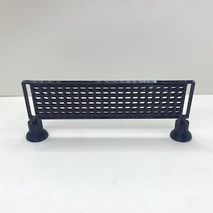 May include: A black rectangular barrier with a grid pattern, featuring a horizontal fence-like structure supported by two circular, pedestal-style bases on each end. The object is constructed with a uniform lattice design and a smooth finish.