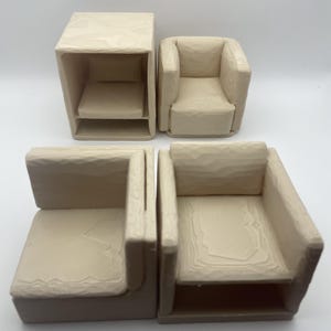 Puede incluir: Un conjunto de cuatro sillones pequeños de color beige y una mesa auxiliar a juego. Los muebles tienen un acabado tallado y texturizado, lo que sugiere un trabajo artesanal. Las sillas tienen un diseño sencillo y moderno, adecuado para una casa de muñecas o una exhibición decorativa.
