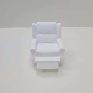 May include: A small, white miniature recliner chair with a footrest. The chair has a detailed design, including armrests and a headrest. The overall aesthetic is clean and modern, with a focus on the chair's form and structure.