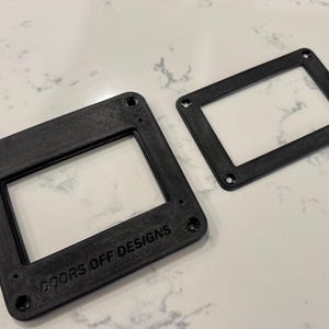May include: Two black rectangular frames with rounded corners and screw holes. One frame is larger than the other. The larger frame has the text "DOORS OFF DESIGNS" printed on it. The frames are made of a matte black material.