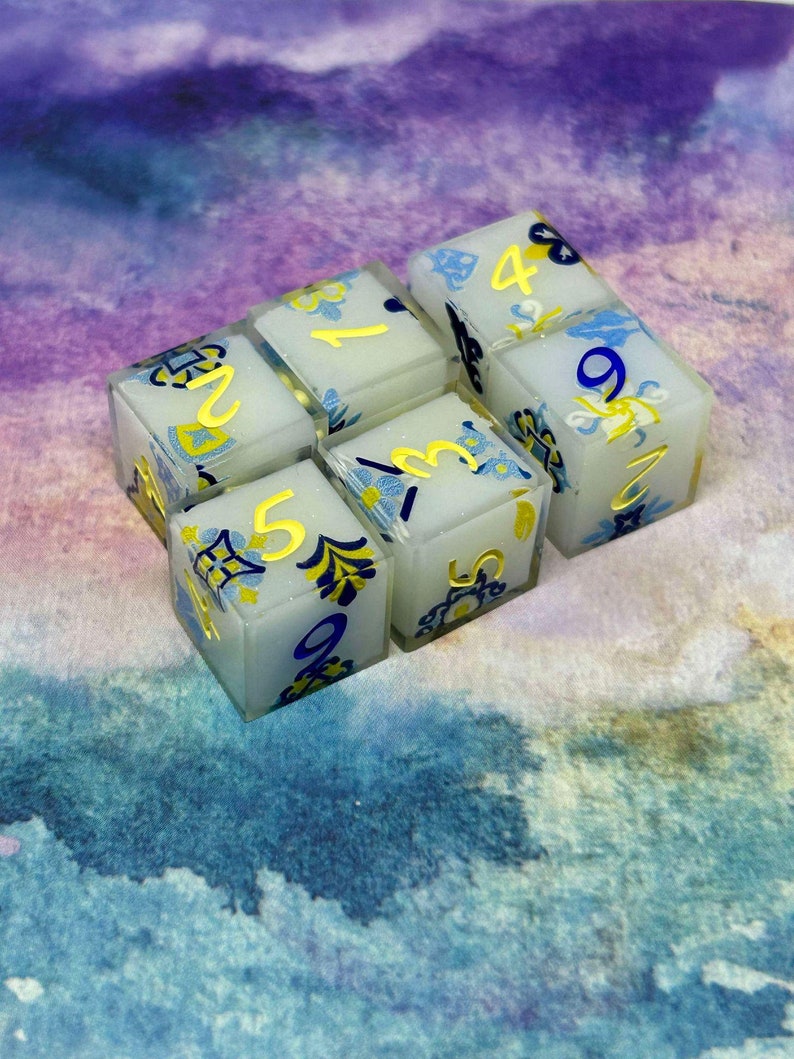 May include: Six white dice with blue and gold accents. Each die has a different number from 1 to 6 printed on it in gold.
