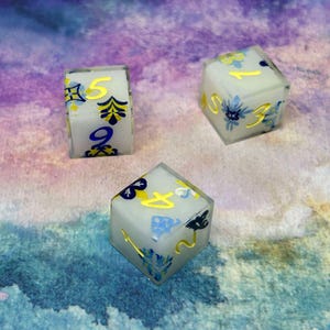 May include: Three white dice with blue and yellow floral designs and gold numbers. The dice are on a purple and blue watercolour background.