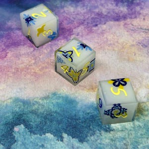 May include: Three white dice with blue and yellow floral designs and gold numbers. The dice are on a purple and blue watercolour background.