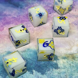 May include: Set of six white dice with yellow numbers and blue floral designs. The dice are opaque and have a frosted finish.