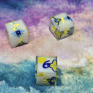 May include: Three white dice with blue and gold floral designs. The dice show the numbers 1, 2, and 6.