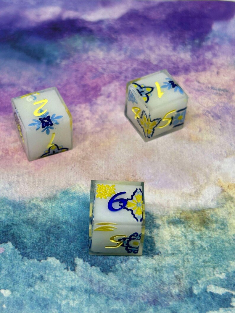 May include: Three white dice with blue and gold floral designs. The dice show the numbers 1, 2, and 6.
