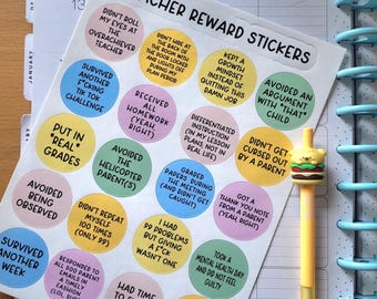 May include: Teacher reward stickers with various phrases like "Survived Another F*cking Tik Tok Challenge" and "Didn't Lose My Sh*t." A yellow pen with a burger topper rests beside the stickers on a planner.