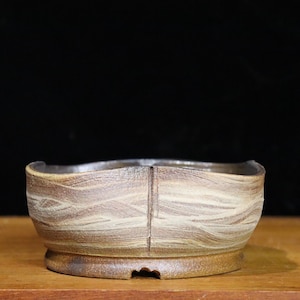 May include: A small, handcrafted ceramic bowl with a unique, textured surface. The bowl features a wave-like pattern in shades of brown and tan. It has a rounded base and a slightly irregular rim, suggesting a handmade origin.