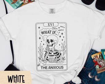Puede incluir: Camiseta blanca con un diseño de carta del tarot en blanco y negro. El diseño presenta un esqueleto, las palabras "WHAT IF..." y "THE ANXIOUS". La camiseta se combina con vaqueros azules y cartas del tarot.