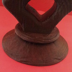 May include: A dark brown wooden base with a unique, abstract design. The base is circular with a raised, textured rim.