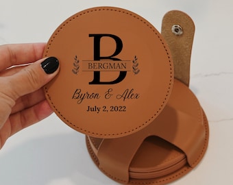 Könnte beinhalten: Satz mit vier braunen Lederuntersetzern mit einem Halter. Der oberste Untersetzer zeigt ein personalisiertes Design mit dem Buchstaben "B", dem Namen "Bergman" und dem Text "Byron & Alex July 2, 2022".