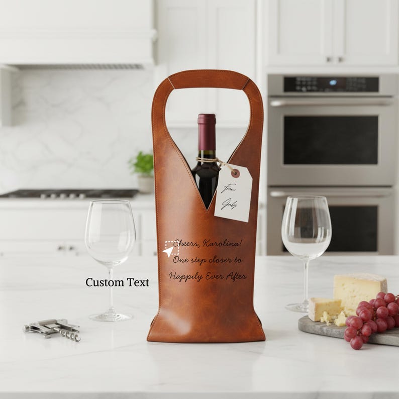 Personalized leather wine tote bag with custom engraved text and gift tag, displayed with wine glasses, cheese, and grapes. Unique wedding, anniversary, or housewarming gift idea