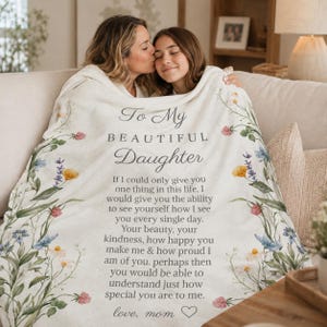 Op de afbeelding: Een crèmekleurige plaid met een bloemenrand van blauwe, gele en roze bloemen. De tekst in het midden luidt: To My BEAUTIFUL Daughter. If I could only give you one thing in this life, I would give you the ability to see yourself how I see.