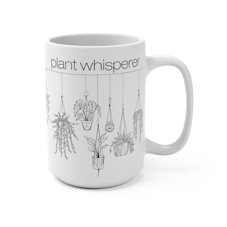 May include: White ceramic mug with a black outline of hanging plants and the text "plant whisperer" on the front.