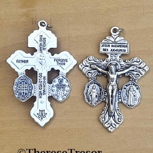 Puede incluir: Dos colgantes religiosos plateados. Un colgante en forma de cruz con las palabras "Padre" y "Perdónalos". El otro colgante representa a Jesús en la cruz, con la inscripción "Jesús Nazarenus Rex Judaeorum."