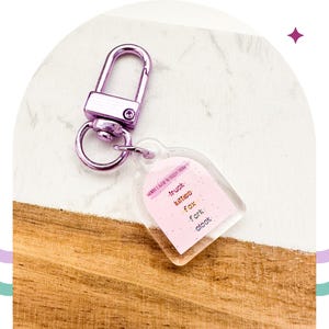 May include: A pink and clear keychain with a silver clasp. The keychain has a pink rectangle with the words "truck kittens fox fork block" written on it.