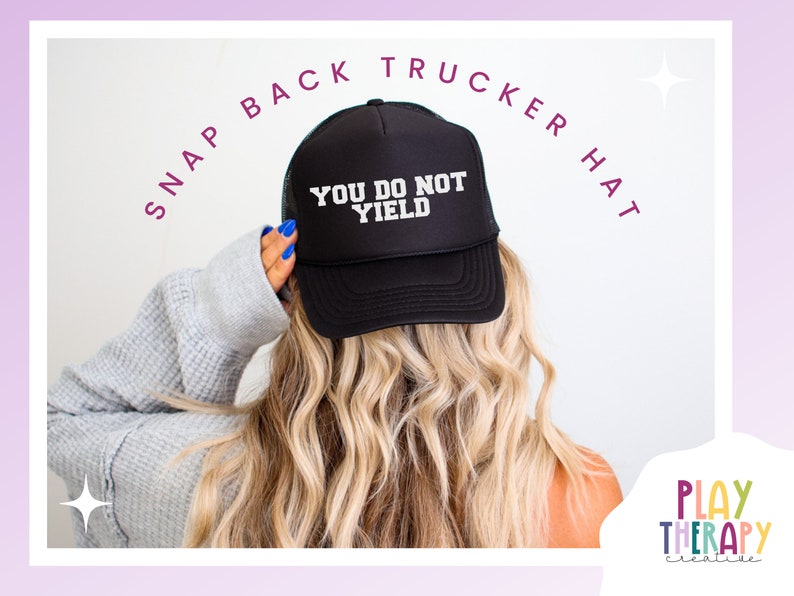 K&ouml;nnte beinhalten: Schwarze Snapback-Trucker-M&uuml;tze mit dem Text "YOU DO NOT YIELD" in Wei&szlig;. Die M&uuml;tze wird von einer Person mit blondem Haar getragen. Die Worte "SNAP BACK TRUCKER HAT" sind &uuml;ber der M&uuml;tze angeordnet. Das Play Therapy Creative-Logo befindet sich unten rechts.