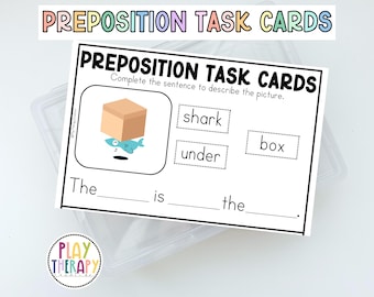 May include: A white task card with the text "PREPOSITION TASK CARDS" and a cartoon illustration of a box and a shark. The card includes fill-in-the-blank sentences to describe the picture. The words "shark", "under", and "box" are also included.